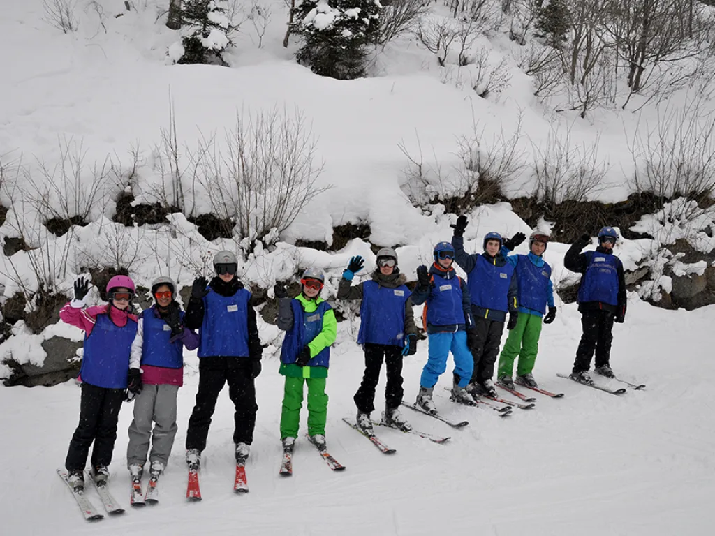 Skigruppe steht in einer Reihe vor einer Schneewand.